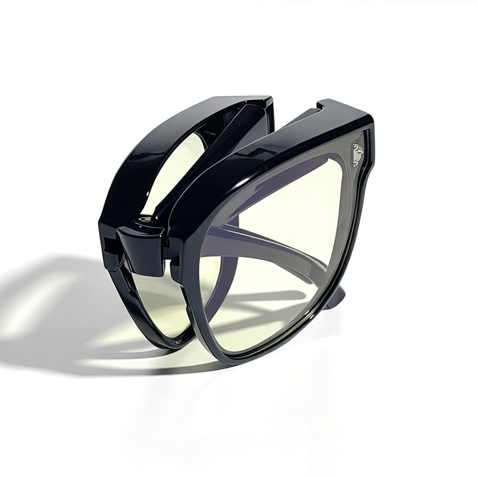Glossy black fit-over night driving glasses with yellow-tinted lenses, fully folded to show the compact foldable temple design.