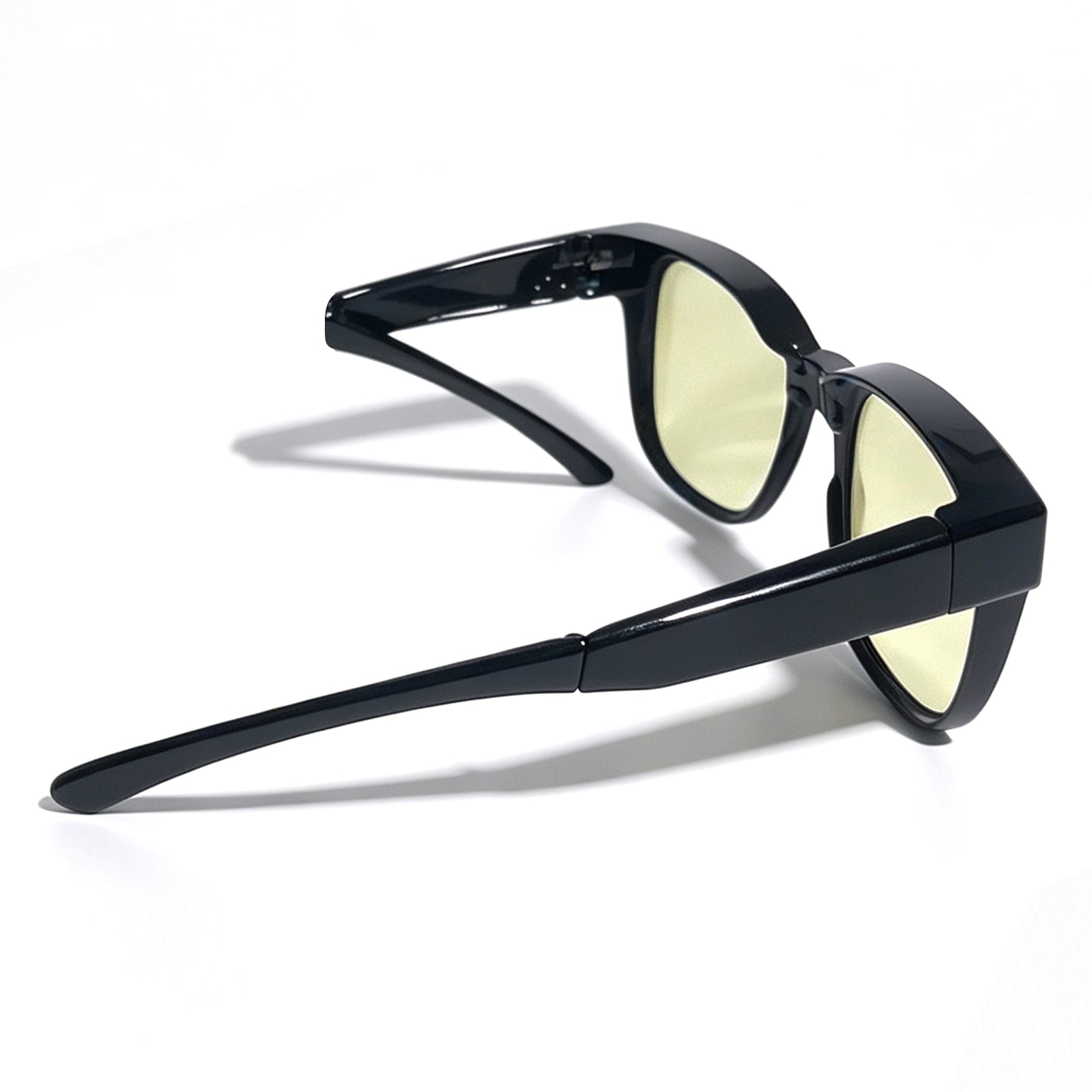 Glossy black fit-over night driving glasses with yellow-tinted lenses, shown from a rear side angle with one temple arm folded to illustrate the foldable temples.