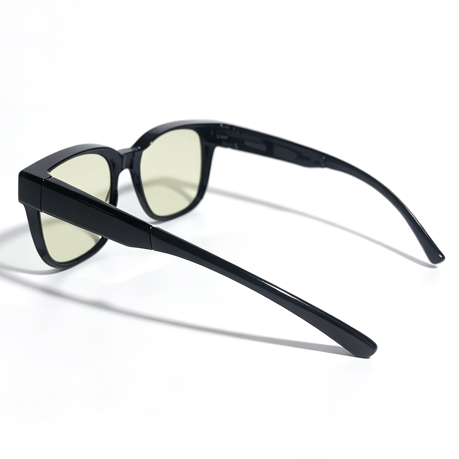 Glossy black fit-over night driving glasses with yellow-tinted lenses, shown from a rear three-quarter angle.