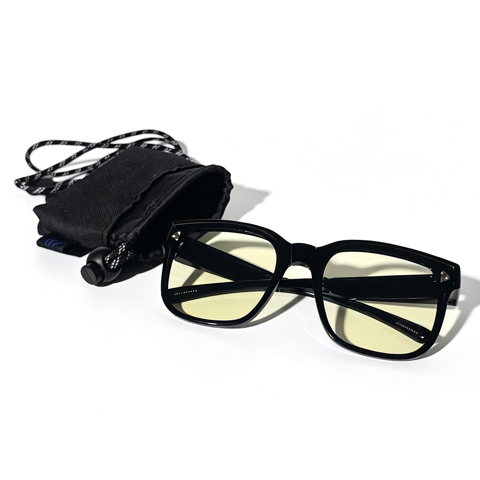 Glossy black fit-over night driving glasses with yellow-tinted lenses shown beside a black drawstring storage pouch.