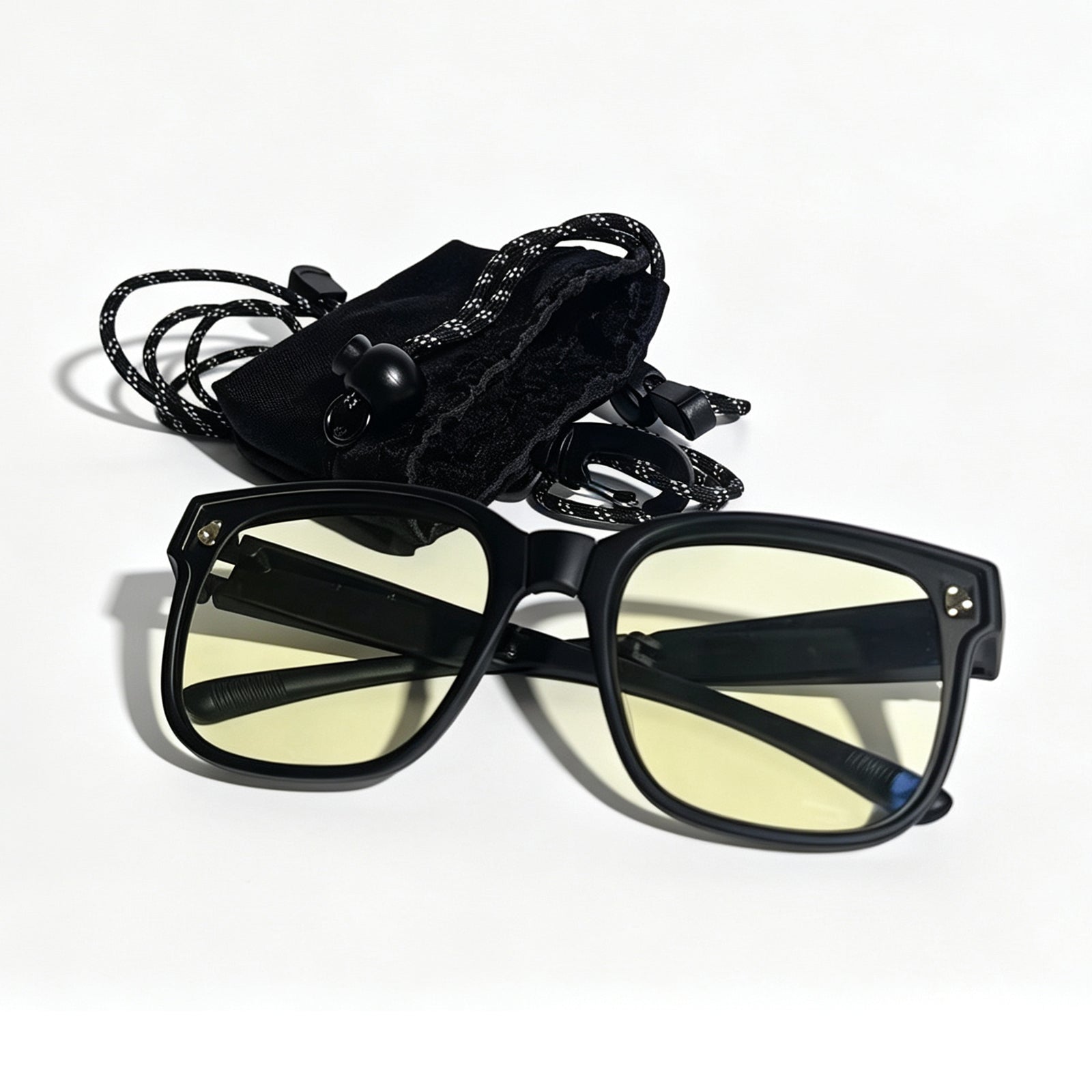 Matte black fit-over night driving glasses with yellow lenses displayed in front of a black storage pouch and adjustable neck strap.