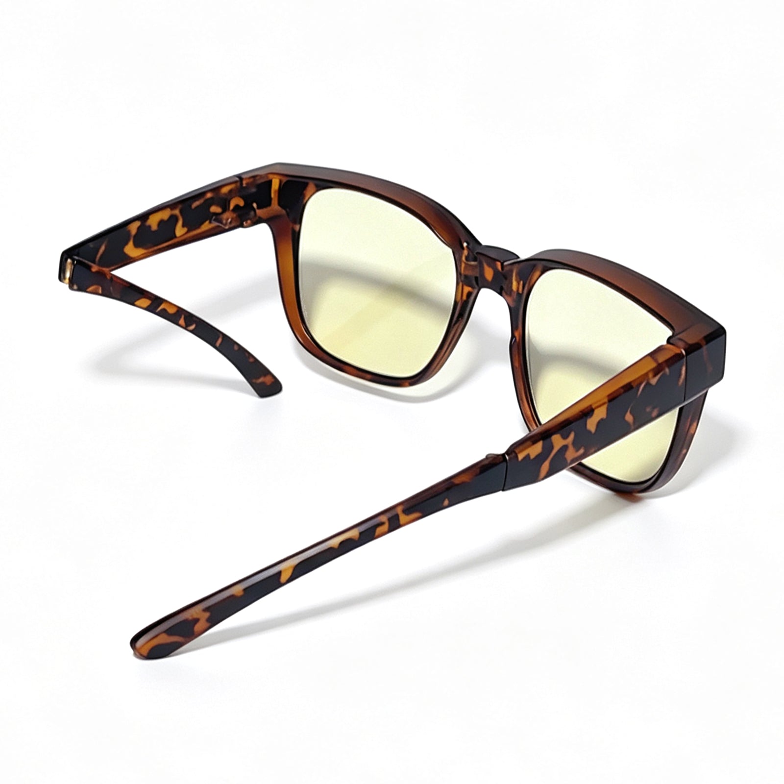 Tortoiseshell fit-over night driving glasses with yellow-tinted lenses, shown from a rear side angle with one temple arm folded to illustrate the foldable temples