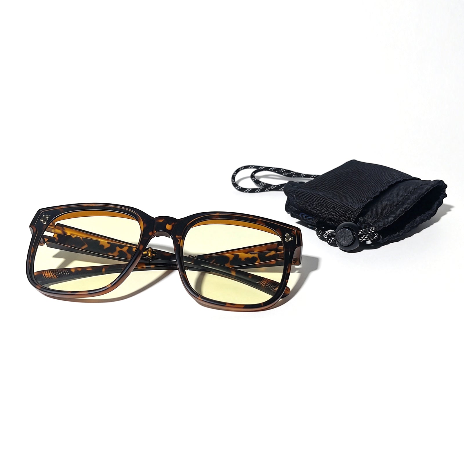 Tortoiseshell fit-over night driving glasses with yellow-tinted lenses shown beside a black drawstring protective pouch.